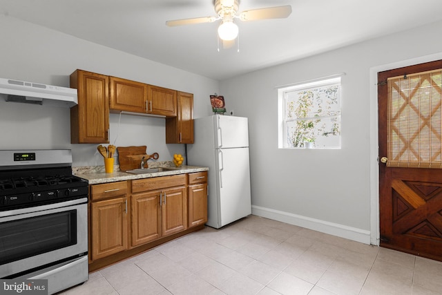 kitchen with wall chimney exhaust hood, sink, stainless steel range with gas cooktop, ceiling fan, and white refrigerator