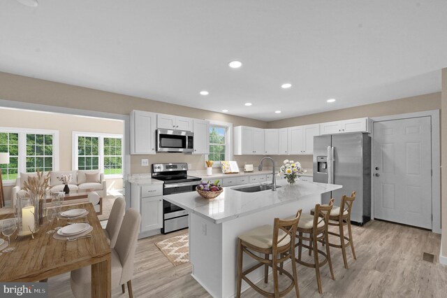 kitchen featuring stainless steel appliances, white cabinets, light wood-type flooring, a center island with sink, and sink