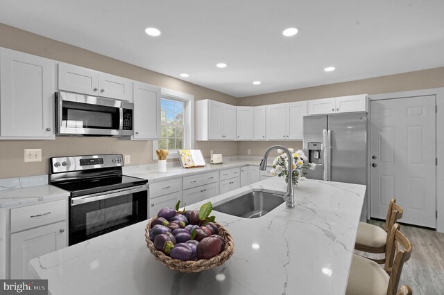 kitchen with light stone counters, white cabinetry, light hardwood / wood-style floors, stainless steel appliances, and sink