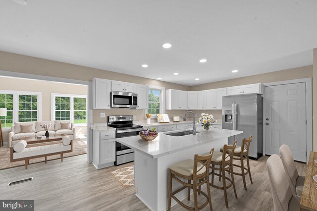 kitchen featuring light wood-type flooring, a breakfast bar area, appliances with stainless steel finishes, white cabinetry, and sink