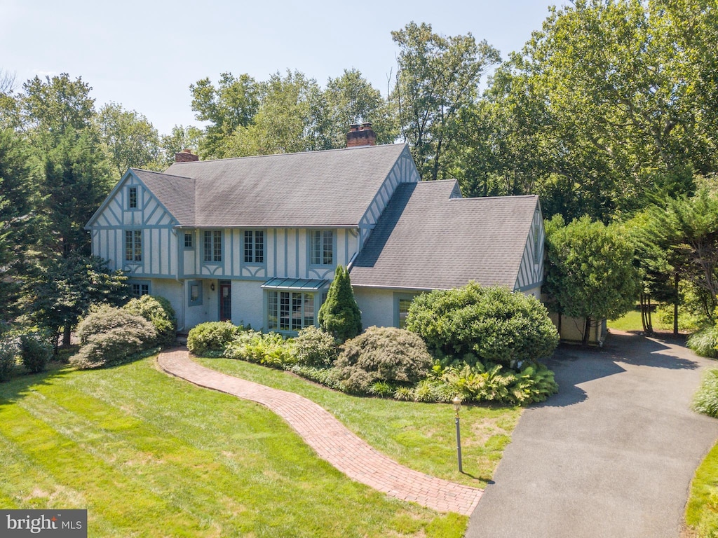 tudor home with aphalt driveway, roof with shingles, a chimney, and a front lawn