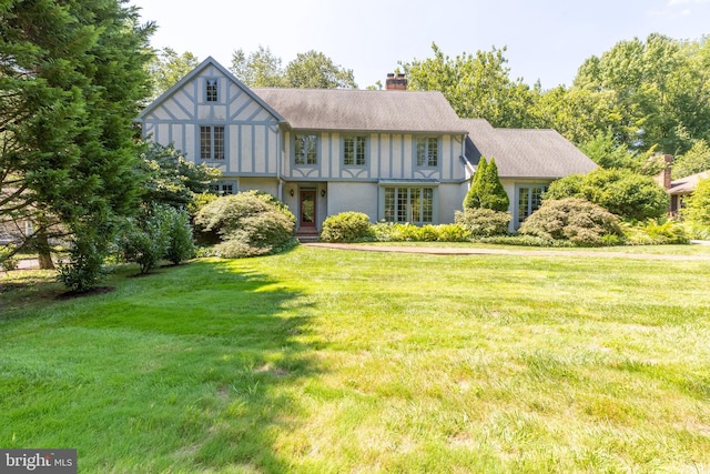 tudor house with a shingled roof, a chimney, a front lawn, and stucco siding