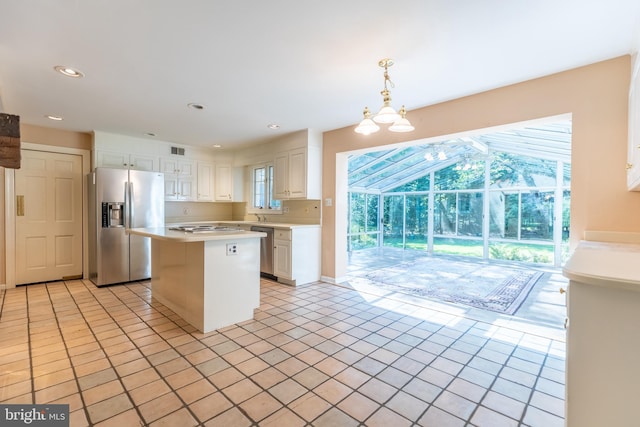 kitchen with light tile patterned flooring, a kitchen island, decorative light fixtures, white cabinets, and stainless steel appliances