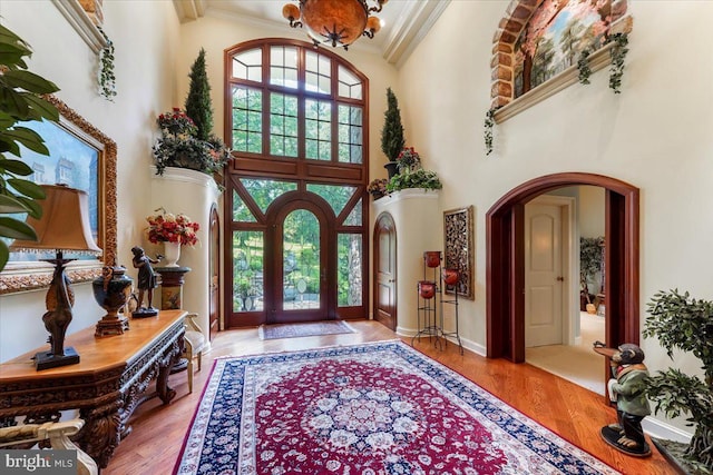 foyer entrance with ornamental molding, arched walkways, a healthy amount of sunlight, and wood finished floors