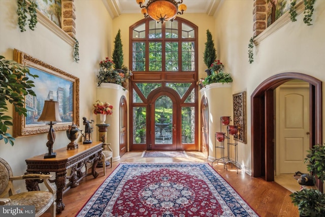 foyer featuring arched walkways, wood finished floors, a high ceiling, crown molding, and a chandelier