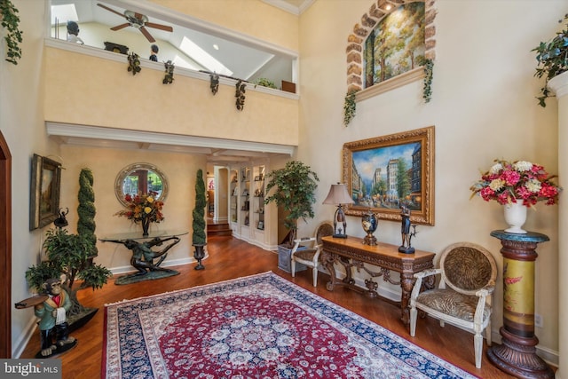 entrance foyer with a ceiling fan, a towering ceiling, baseboards, and wood finished floors