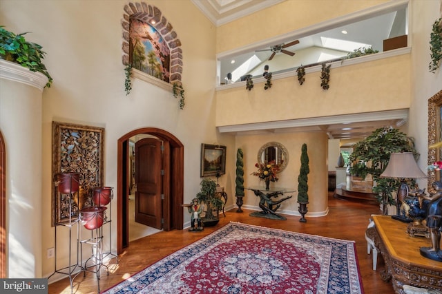 entryway featuring arched walkways, ceiling fan, wood finished floors, a towering ceiling, and ornamental molding