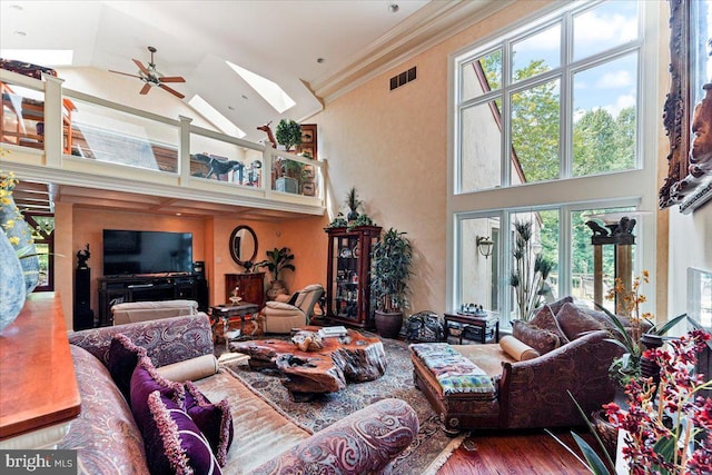 living room featuring a skylight, wood finished floors, a ceiling fan, visible vents, and crown molding