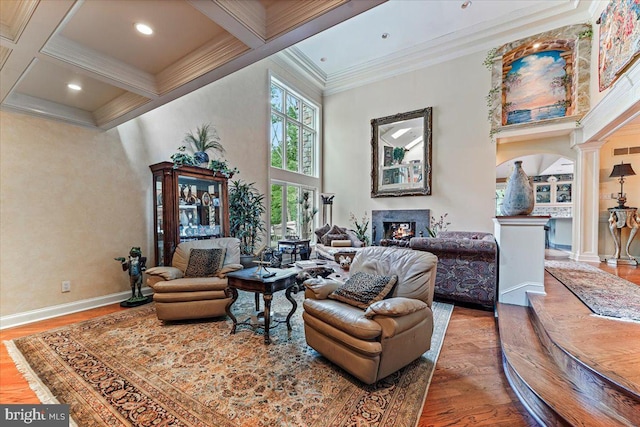 sitting room with a towering ceiling, crown molding, ornate columns, beam ceiling, and a high end fireplace