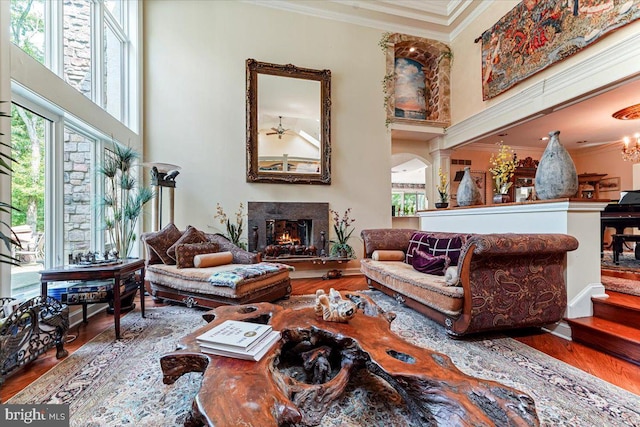 sitting room featuring a warm lit fireplace, a high ceiling, wood finished floors, and crown molding