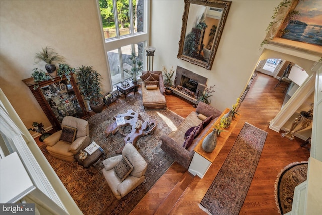 living room with arched walkways, a high ceiling, a fireplace, and wood finished floors