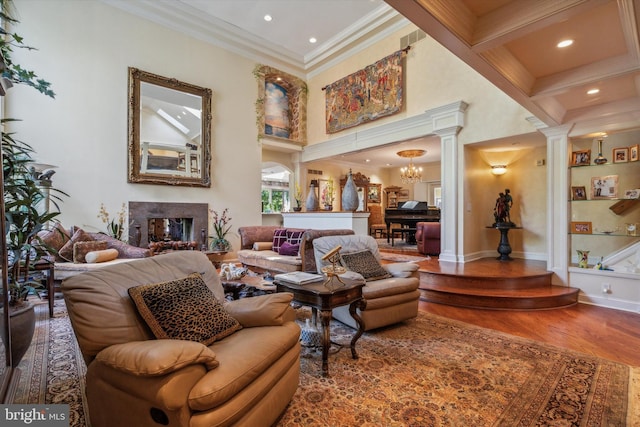 interior space featuring a fireplace, wood finished floors, ornamental molding, ornate columns, and an inviting chandelier