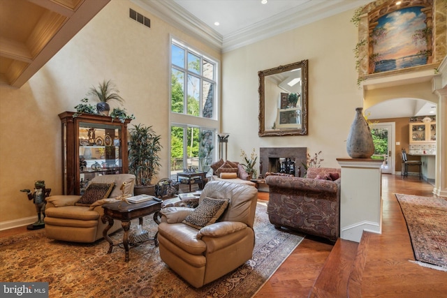 sitting room with visible vents, a towering ceiling, ornamental molding, wood finished floors, and a fireplace