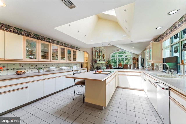 kitchen featuring light tile patterned floors, tasteful backsplash, lofted ceiling, a peninsula, and dishwashing machine