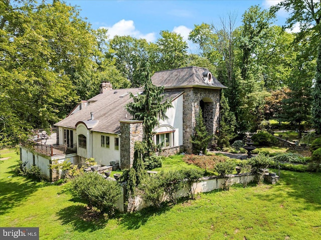 exterior space featuring stone siding, a chimney, a front lawn, and stucco siding