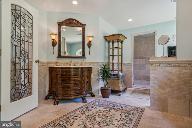 bathroom with walk in shower, wainscoting, vanity, and tile walls