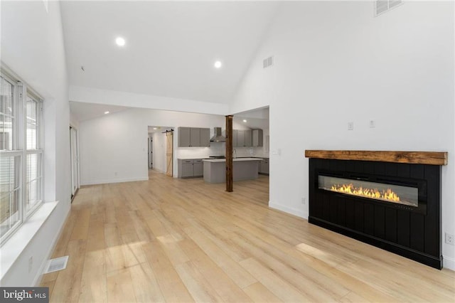 unfurnished living room featuring light hardwood / wood-style flooring, a wealth of natural light, and high vaulted ceiling