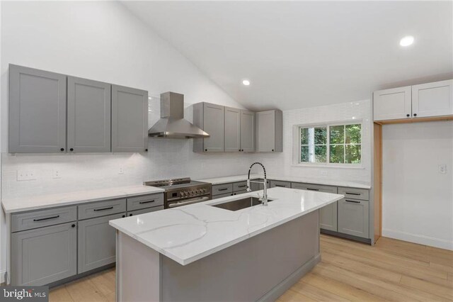 kitchen with wall chimney range hood, sink, light hardwood / wood-style floors, lofted ceiling, and high end stainless steel range