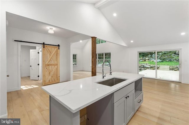 kitchen featuring light wood-type flooring, light stone counters, a barn door, an island with sink, and sink