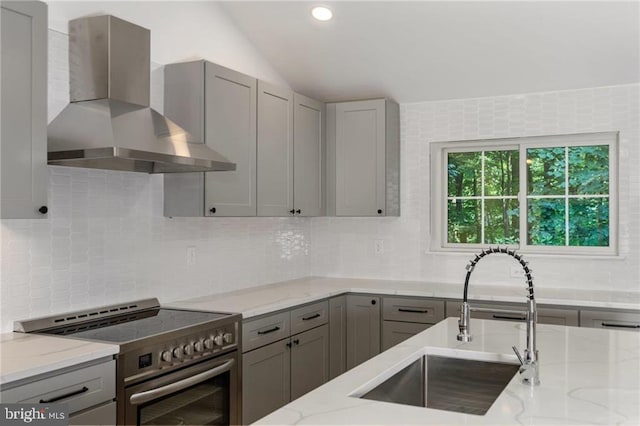 kitchen with tasteful backsplash, wall chimney exhaust hood, sink, and high end stove