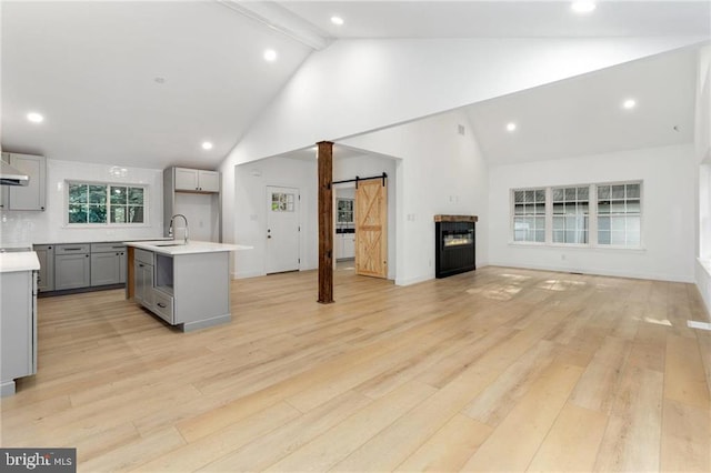 kitchen featuring gray cabinets, high vaulted ceiling, beamed ceiling, a barn door, and light hardwood / wood-style flooring