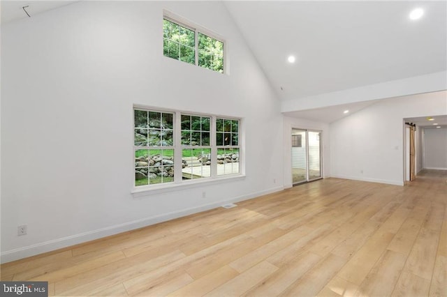 spare room with plenty of natural light, high vaulted ceiling, and light hardwood / wood-style flooring