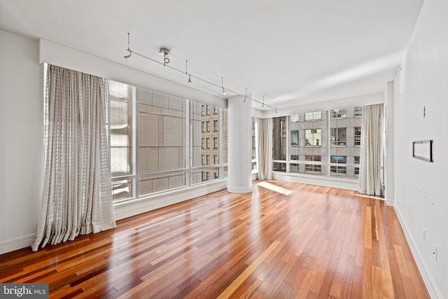 interior space featuring wood-type flooring, a wealth of natural light, decorative columns, and rail lighting