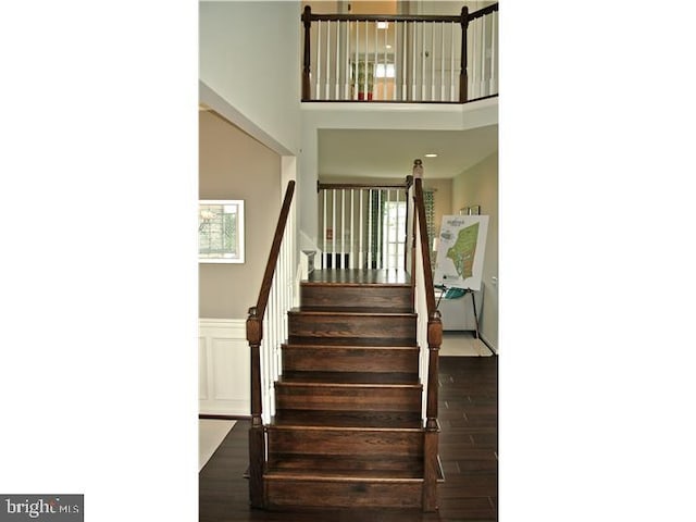 staircase featuring a decorative wall, a wainscoted wall, a high ceiling, and wood finished floors