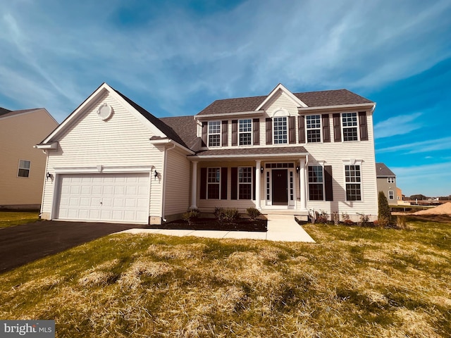 colonial home with aphalt driveway, a front yard, an attached garage, and a shingled roof