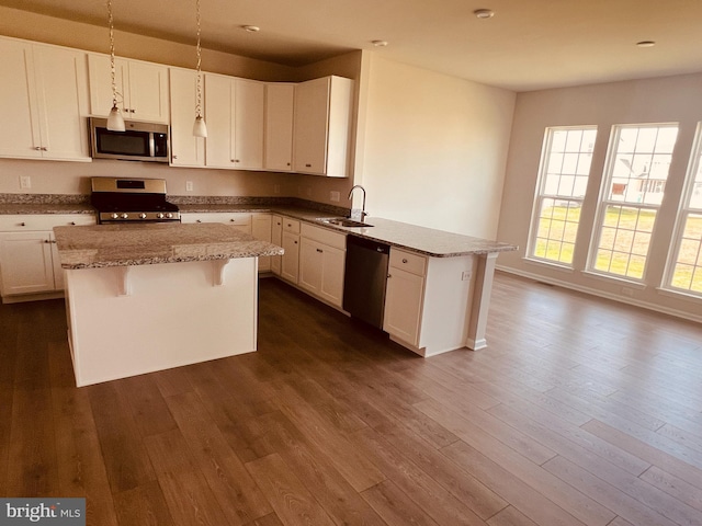 kitchen featuring appliances with stainless steel finishes, a peninsula, dark wood-style floors, white cabinets, and a sink