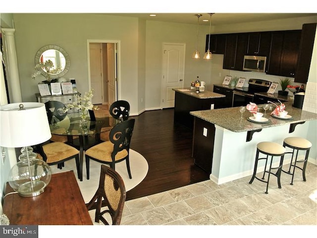 kitchen featuring a kitchen breakfast bar, light hardwood / wood-style flooring, hanging light fixtures, stainless steel appliances, and kitchen peninsula