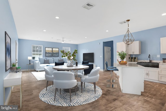 dining space featuring wood-type flooring, sink, and ceiling fan with notable chandelier