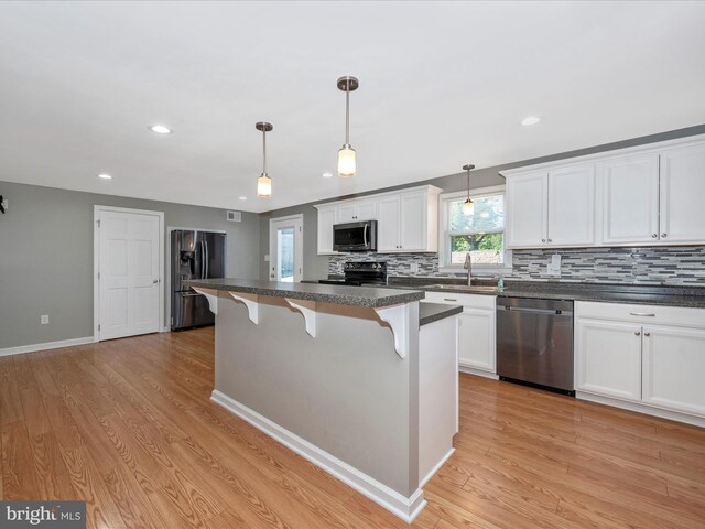 kitchen with sink, a kitchen island, pendant lighting, stainless steel appliances, and white cabinets