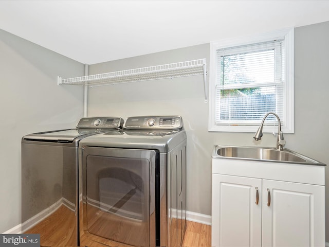 clothes washing area featuring cabinets, washer and clothes dryer, sink, and light wood-type flooring