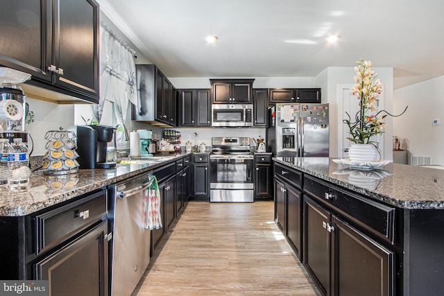 kitchen featuring a sink, appliances with stainless steel finishes, a center island, dark stone counters, and light wood finished floors