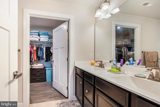 bathroom featuring a walk in closet, visible vents, a sink, and double vanity