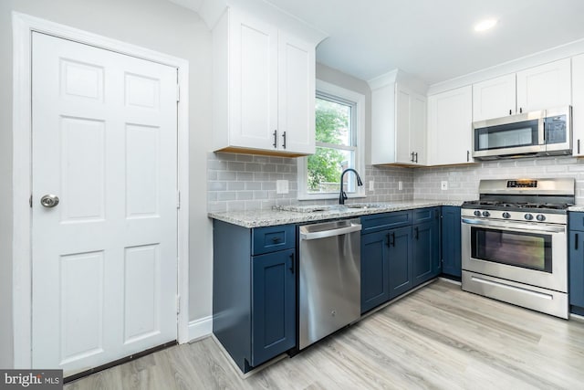 kitchen with sink, white cabinetry, blue cabinetry, stainless steel appliances, and light hardwood / wood-style floors