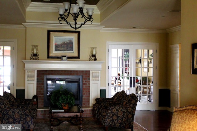 living room with ornamental molding, hardwood / wood-style flooring, a notable chandelier, and a brick fireplace