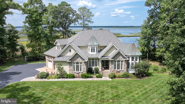 craftsman-style house featuring a garage, a water view, driveway, stone siding, and a front yard