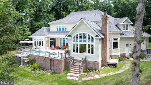 back of property featuring crawl space, a chimney, an outdoor pool, and a yard