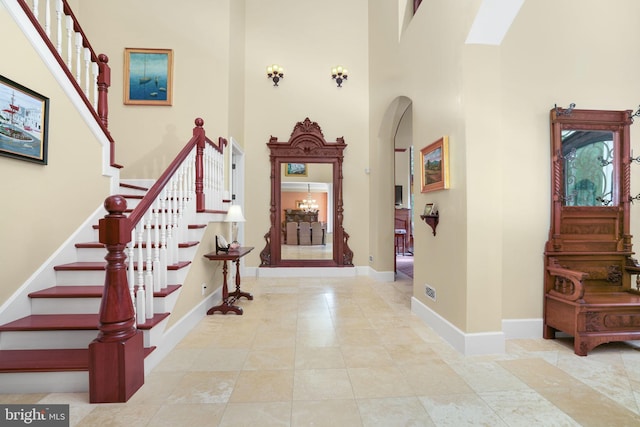 entrance foyer featuring a towering ceiling, stairway, baseboards, and arched walkways