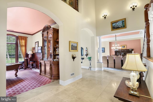 entrance foyer featuring crown molding, a towering ceiling, baseboards, decorative columns, and an inviting chandelier