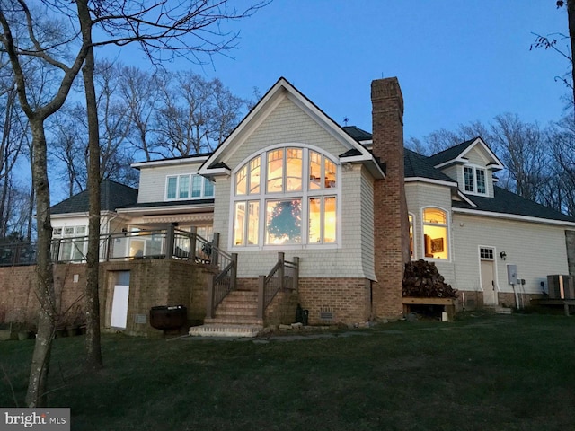 back house at dusk with a lawn and central AC