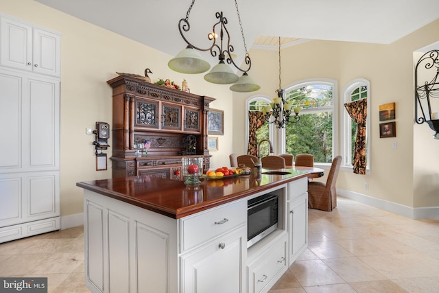 kitchen featuring a kitchen island, stainless steel microwave, hanging light fixtures, white cabinetry, and a sink