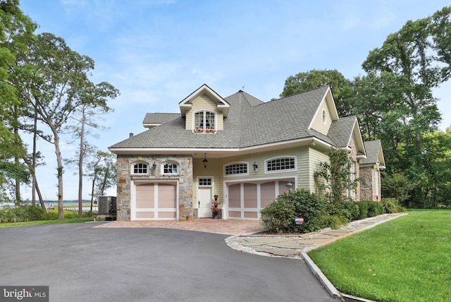 view of front of property with decorative driveway, a garage, cooling unit, stone siding, and a front lawn