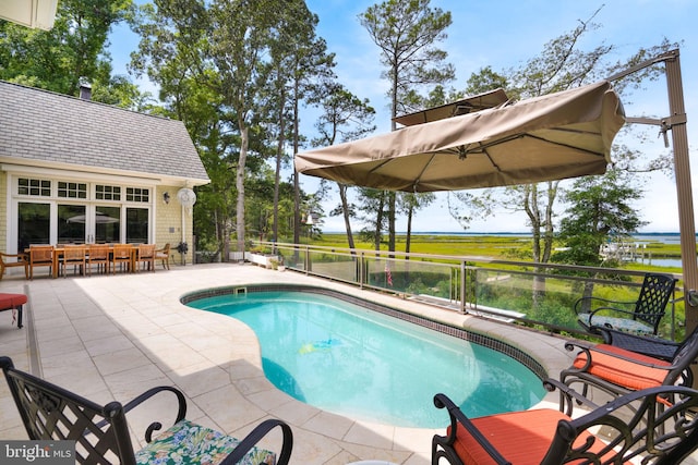 outdoor pool featuring a patio area, a water view, and fence