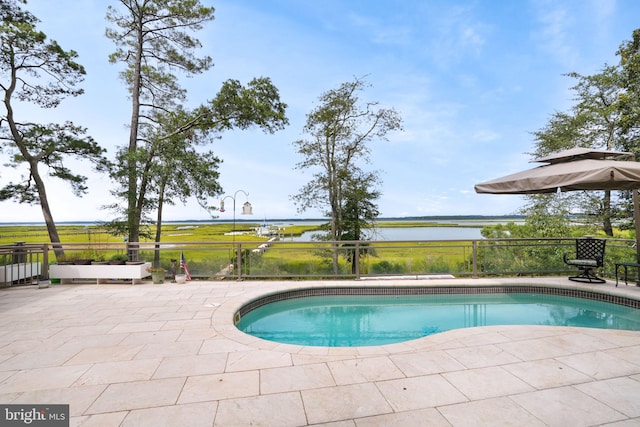 outdoor pool with a patio area, a water view, and fence