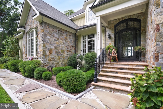 view of exterior entry featuring stone siding and roof with shingles