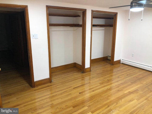 unfurnished bedroom featuring multiple closets, ceiling fan, a baseboard radiator, and light hardwood / wood-style flooring