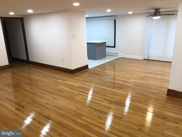 empty room featuring a baseboard heating unit, wood-type flooring, and ceiling fan